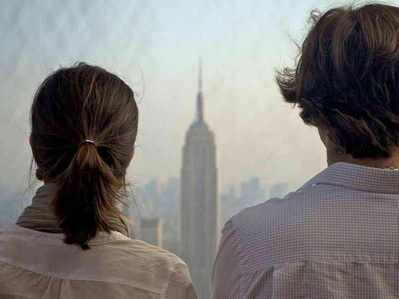 Two people shot from the back standing next to each other. In between them, you can see out over NYC.
